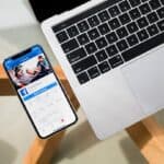 Smartphone mit geöffneter Facebook-Seite liegt auf einem Holztisch neben einem MacBook-Laptop - Seeberger Marketing
