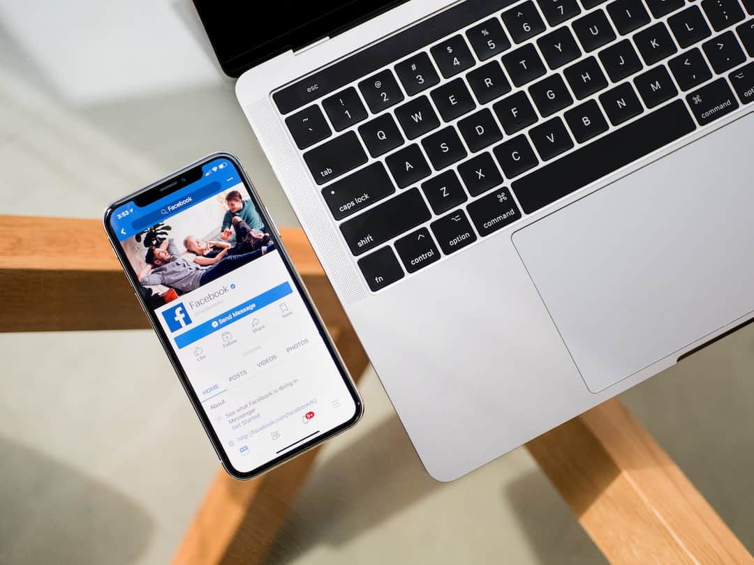 Smartphone mit geöffneter Facebook-Seite liegt auf einem Holztisch neben einem MacBook-Laptop - Seeberger Marketing